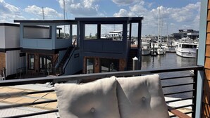 A balcony with a view of a marina, a staircase, and a building with a wooden facade. - Palm Springs at The Cove Riverwalk Villas (Wilmington)