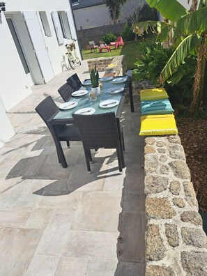 An outdoor patio with a glass-top table set for dining, wicker chairs, and a stone wall.