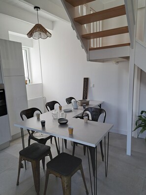 A modern kitchen with a white table, black chairs, and a hanging light fixture.