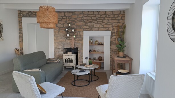 Una sala de estar con pared de piedra, un sofá, dos sillones, una mesita y una lámpara colgante.