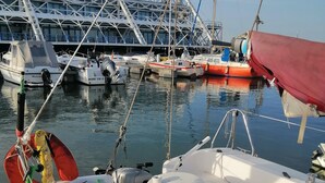A marina with boats docked, a bridge in the background, and a white boat with a table and cushions.