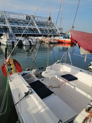 A marina with boats docked, a bridge in the background, and a white boat with a table and cushions.
