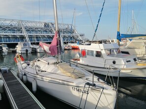 A marina with several boats docked, a bridge structure in the background, and a clear sky.