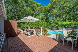 Um deck de madeira com área de estar externa, piscina e vegetação exuberante.