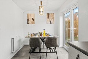 A dining area with a table set for two, a radiator, and artwork on the wall. - Family-Friendly 3BR Home with Games (Blackburn with Darwen)
