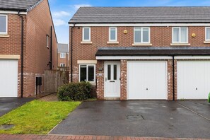 Une maison à deux étages, construite en briques, avec un garage, une porte d’entrée et un petit jardin devant.