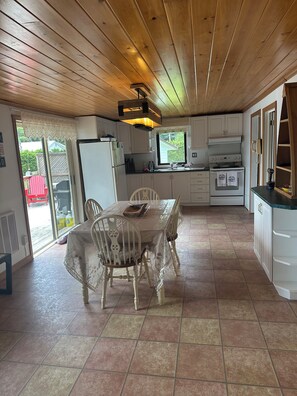 A kitchen with wooden ceiling, white cabinets, a dining table with chairs, and a view through a sliding glass door. - Family Retreat in Beautiful Seguin (Seguin)