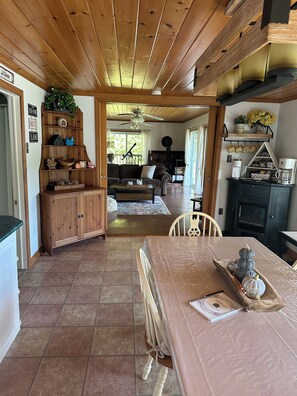 Un intérieur chaleureux avec un plafond en bois, un coin repas avec une table et des chaises, une cuisine équipée de placards et un salon avec un canapé et une cheminée.