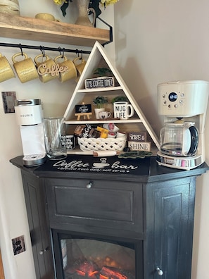 A coffee station with a Keurig coffee maker, a coffee bar sign, and a mug life display.