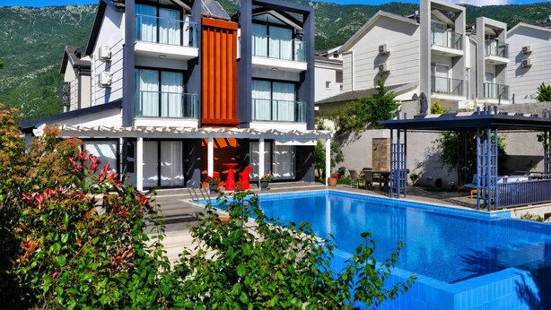 A modern two-story hotel with a swimming pool, outdoor seating, and mountain views.