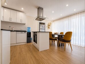 A modern kitchen with white cabinets, a built-in oven, a water dispenser, and a stainless steel range hood. - The Villa Premium Rose in Oludeniz (Muğla)