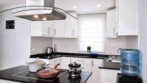 A modern kitchen with white cabinets, a black countertop, a stainless steel range hood, a kettle, a coffee maker, a water dispenser, and a pot on the stove.