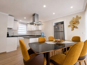 A modern kitchen with white cabinets, a stainless steel refrigerator, and a dining table with four chairs. - The Villa Premium Rose in Oludeniz (Muğla)