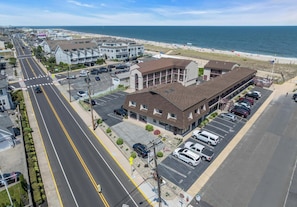 Un hotel frente al mar con estacionamiento, una calle con paso de peatones y una playa al fondo.