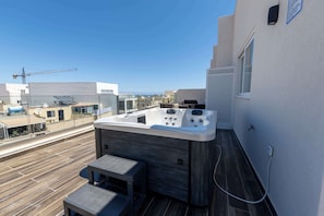 Eine Dachterrasse mit Whirlpool, einer Holzterrasse und Blick auf die Stadt.