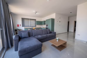 Ein modernes Wohnzimmer mit einem Ecksofa, einem Couchtisch aus Holz und einer Küche im Hintergrund.