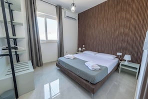Ein modernes Hotelzimmer mit Bett, Nachttisch, Lampe, Klimaanlage und einem fenster mit Vorhängen.