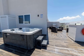 Eine Dachterrasse mit Whirlpool, Gartenmöbeln und Blick auf die Stadt.