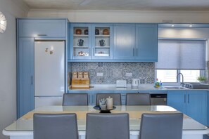 A modern kitchen with blue cabinets, a refrigerator, a coffee station, and a dining area with chairs. - Ghajnsielem 3BDR Flat with Views - NO Lift (Għajnsielem)