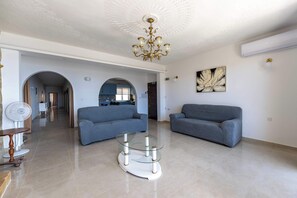 A spacious living room with two sofas, a glass coffee table, a chandelier, and a painting on the wall. - Ghajnsielem 3BDR Flat with Views - NO Lift (Għajnsielem)