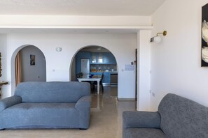A living room with a sofa, a dining table, and a kitchen in the background. - Ghajnsielem 3BDR Flat with Views - NO Lift (Għajnsielem)