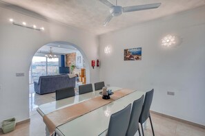 A modern dining area with a glass table, chairs, and a ceiling fan. - Ghajnsielem 3BDR Flat with Views - NO Lift (Għajnsielem)