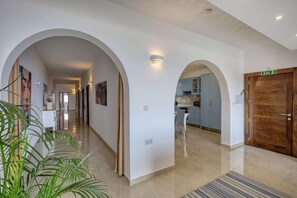 A hotel corridor with arched doorways, a visible exit sign, and a kitchen area in the background. - Ghajnsielem 3BDR Flat with Views - NO Lift (Għajnsielem)