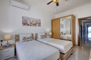 A hotel room with two beds, a ceiling fan, an air conditioning unit, a large mirror, and a view of the sea through an open door. - Ghajnsielem 3BDR Flat with Views - NO Lift (Għajnsielem)