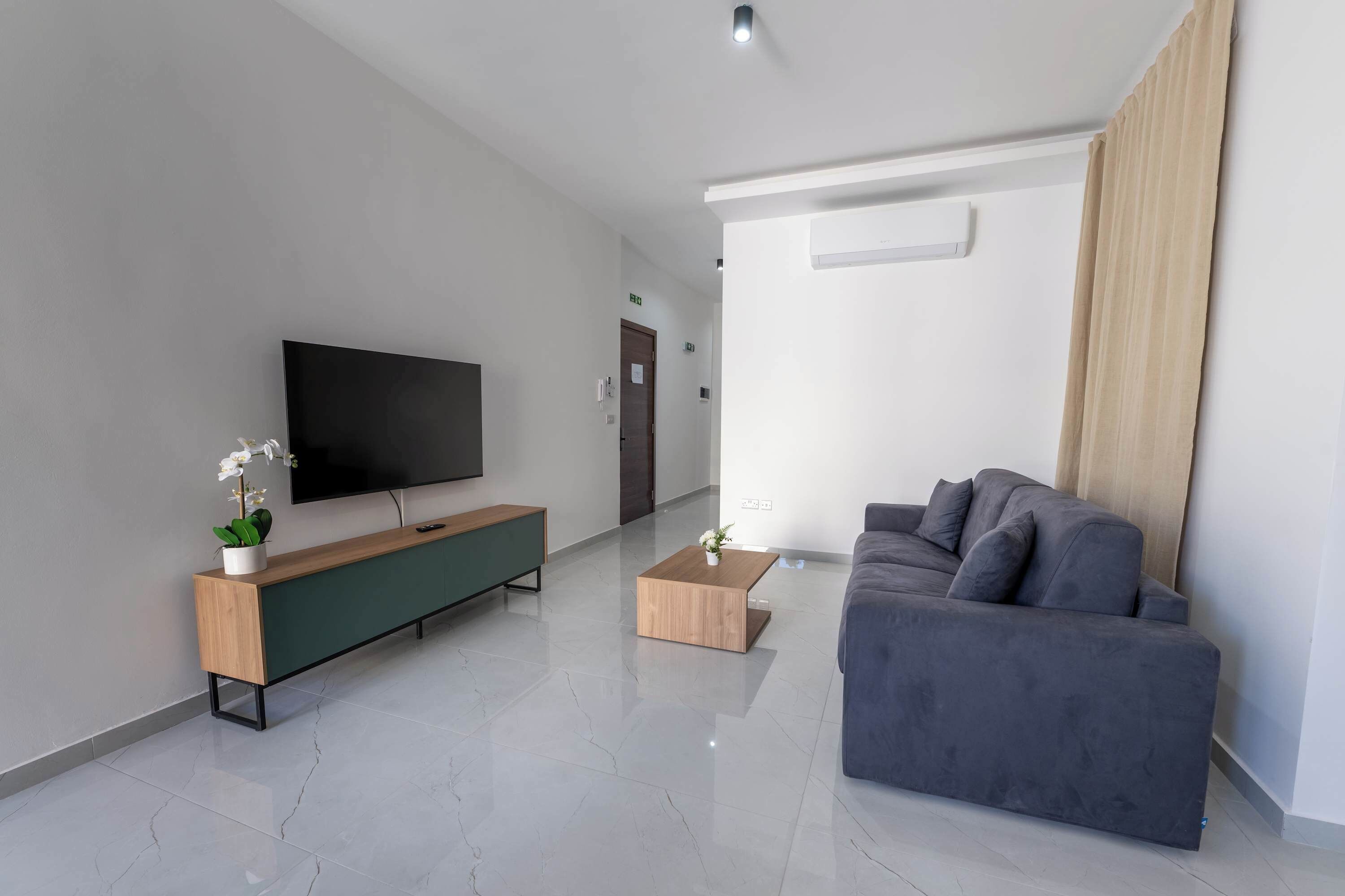 Un soggiorno moderno con una televisione a schermo piatto, un tavolino consolle in legno, un divano grigio e un tavolino da caffè.