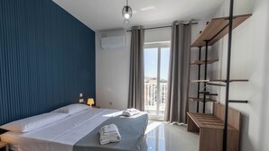Ein modernes Hotelzimmer mit einem großen Bett, einer Holzbank, einem Balkon mit Aussicht und einer Klimaanlage.