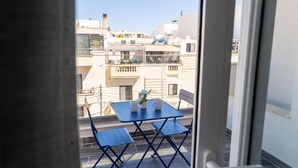 Een balkon met een tafel en stoelen, een bloempot en uitzicht op omliggende gebouwen.