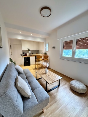 Ein modernes Wohnzimmer mit einem grauen Sofa, einem Holztisch und einer Küche im Hintergrund.