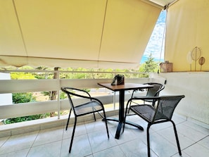 Ein Balkon mit Tisch und Stühlen, Blick ins Grüne und einem weißen Geländer.