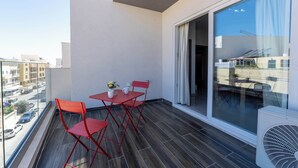 Uma varanda com mesa e cadeiras, vista para a rua e uma janela grande.