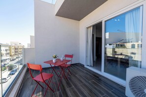Ein Balkon mit Tisch und Stühlen, Blick auf die Straße und ein großes Fenster.