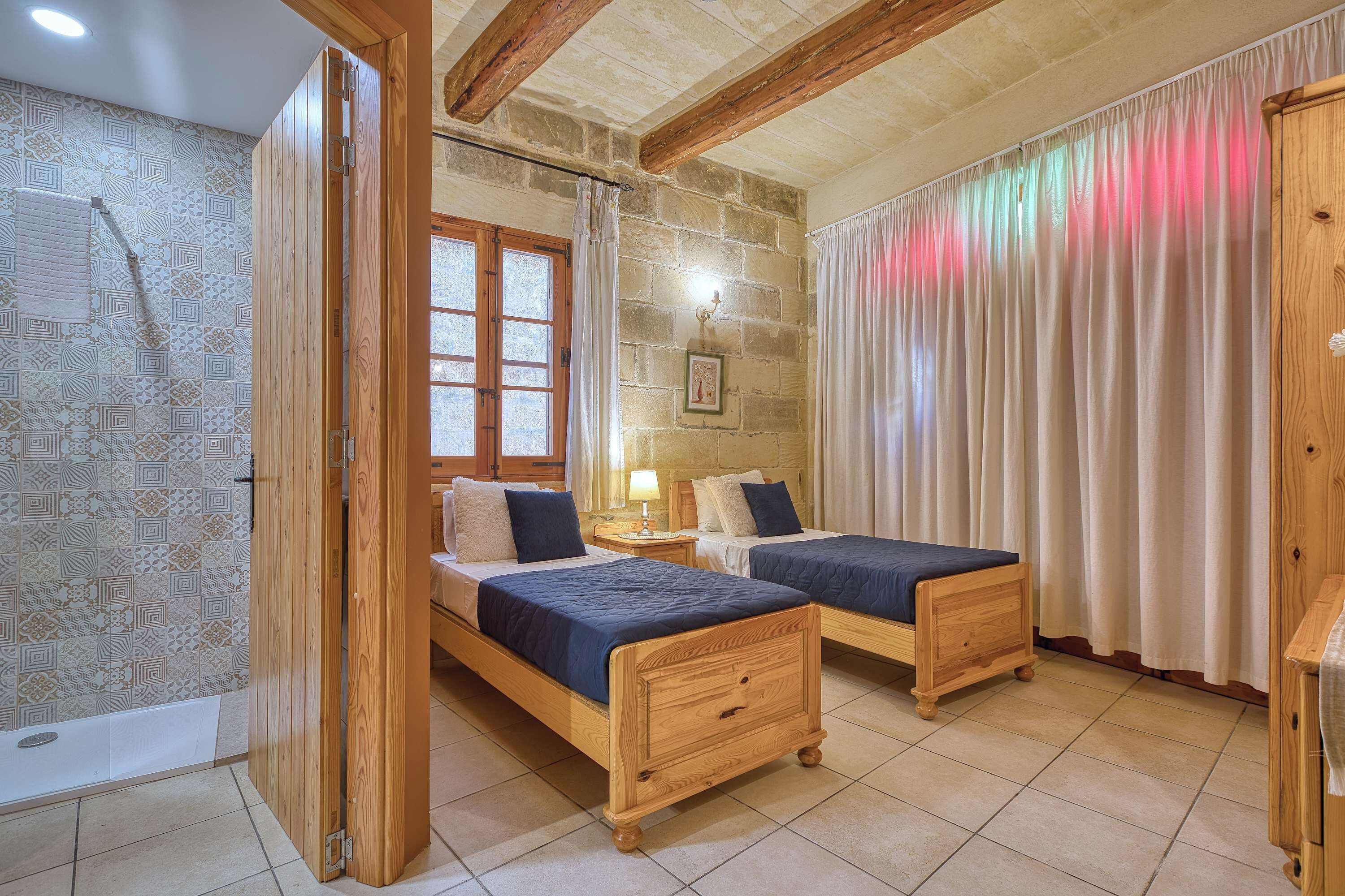 Una habitación con dos camas de madera, una pared de piedra, una ventana con cortinas y un techo de madera.