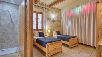 Una habitación con dos camas de madera, una pared de piedra, una ventana con cortinas y un techo de madera.