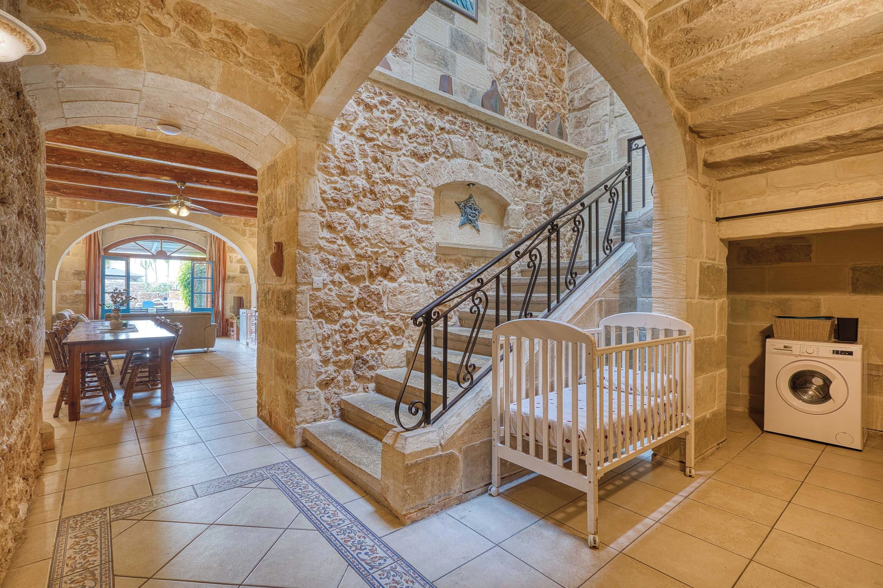 Interior con paredes de piedra, una escalera, zona de comedor y lavadora.