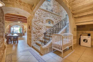 A stone-walled interior with a staircase, a dining area, and a washing machine. - Xaghra 5BDR Farmhouse with Pool by PMI Malta (Ix-Xagħra)