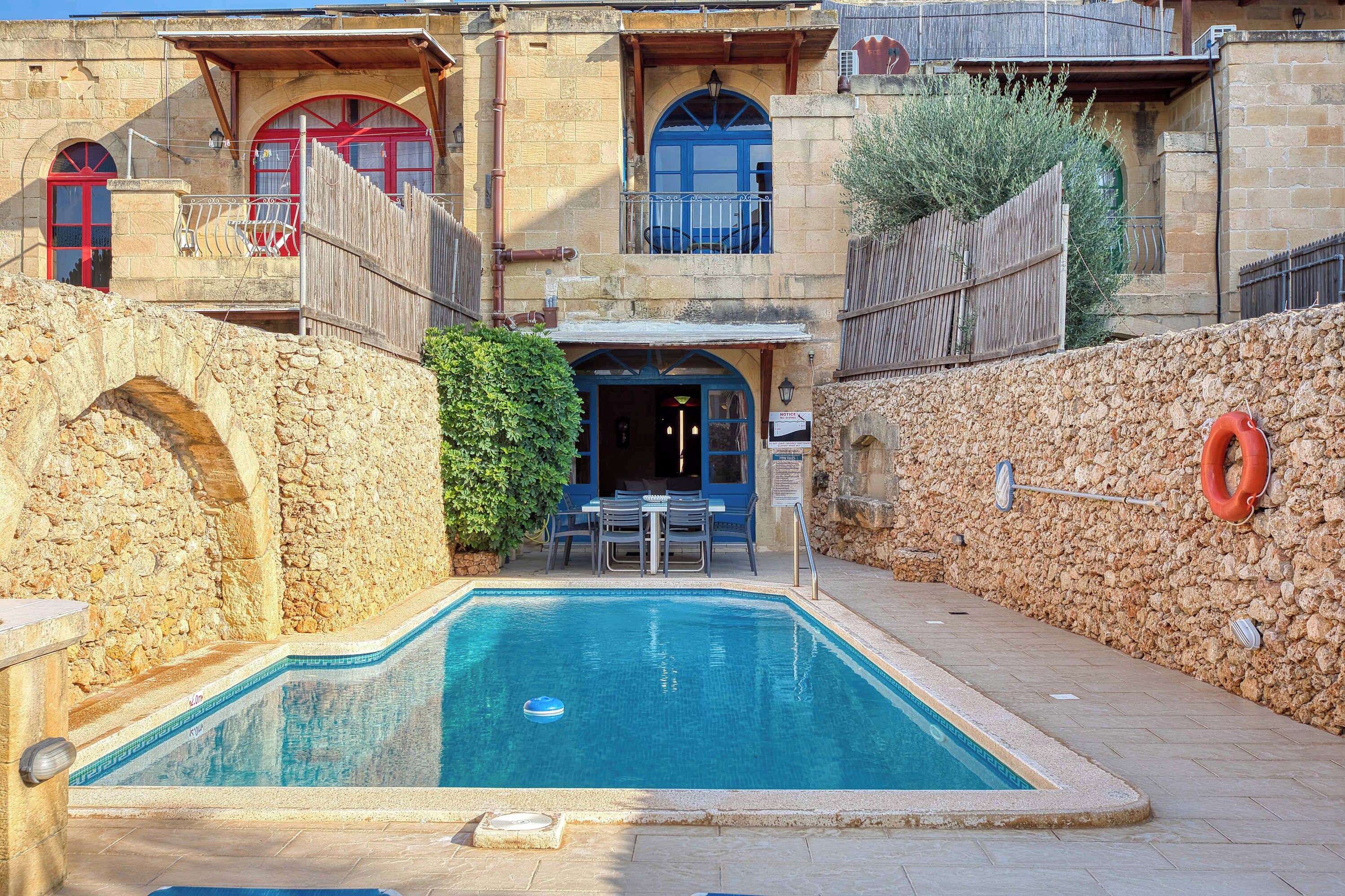 Un edificio de piedra con piscina, mobiliario exterior y un flotador.
