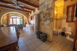 A spacious kitchen with a dining area, stone walls, and a view through an arched doorway.
