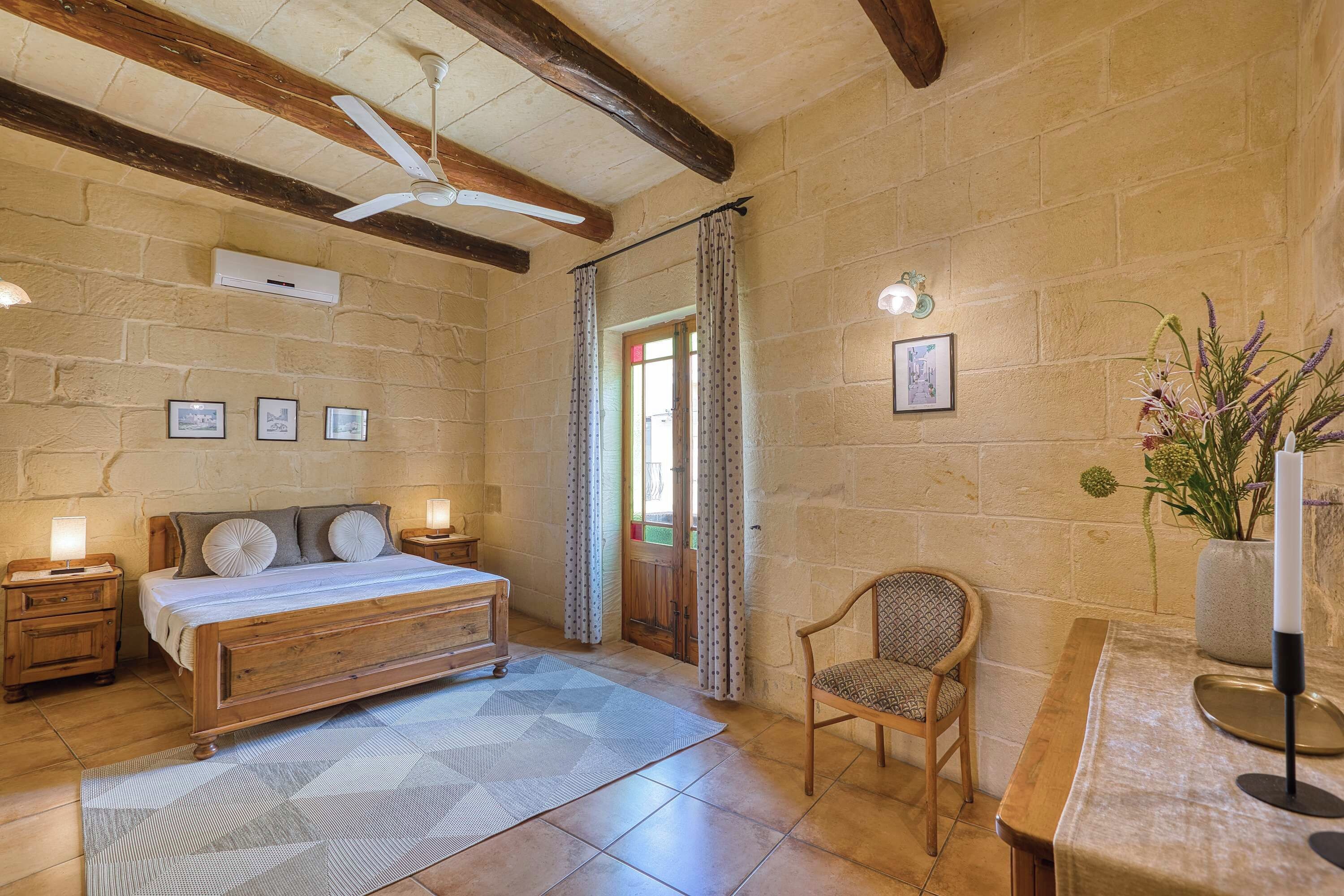 A bedroom with a wooden bed, a chair, a desk, and a ceiling fan.
