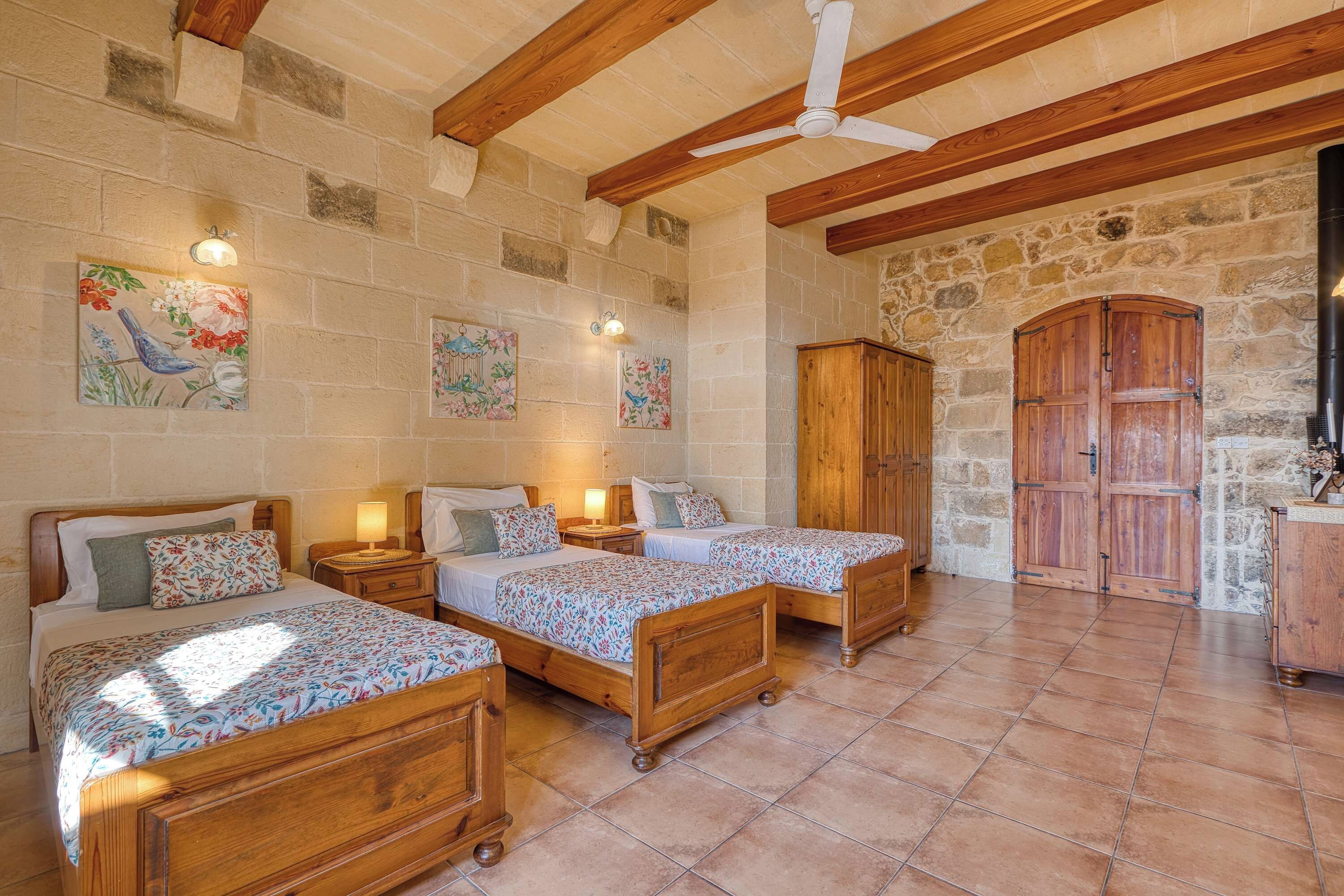 Une pièce avec trois lits en bois, un mur en pierre et une armoire en bois.