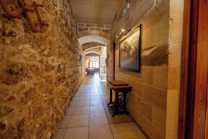 A stone corridor with a wooden bench, a painting on the wall, and an arched doorway in the distance.