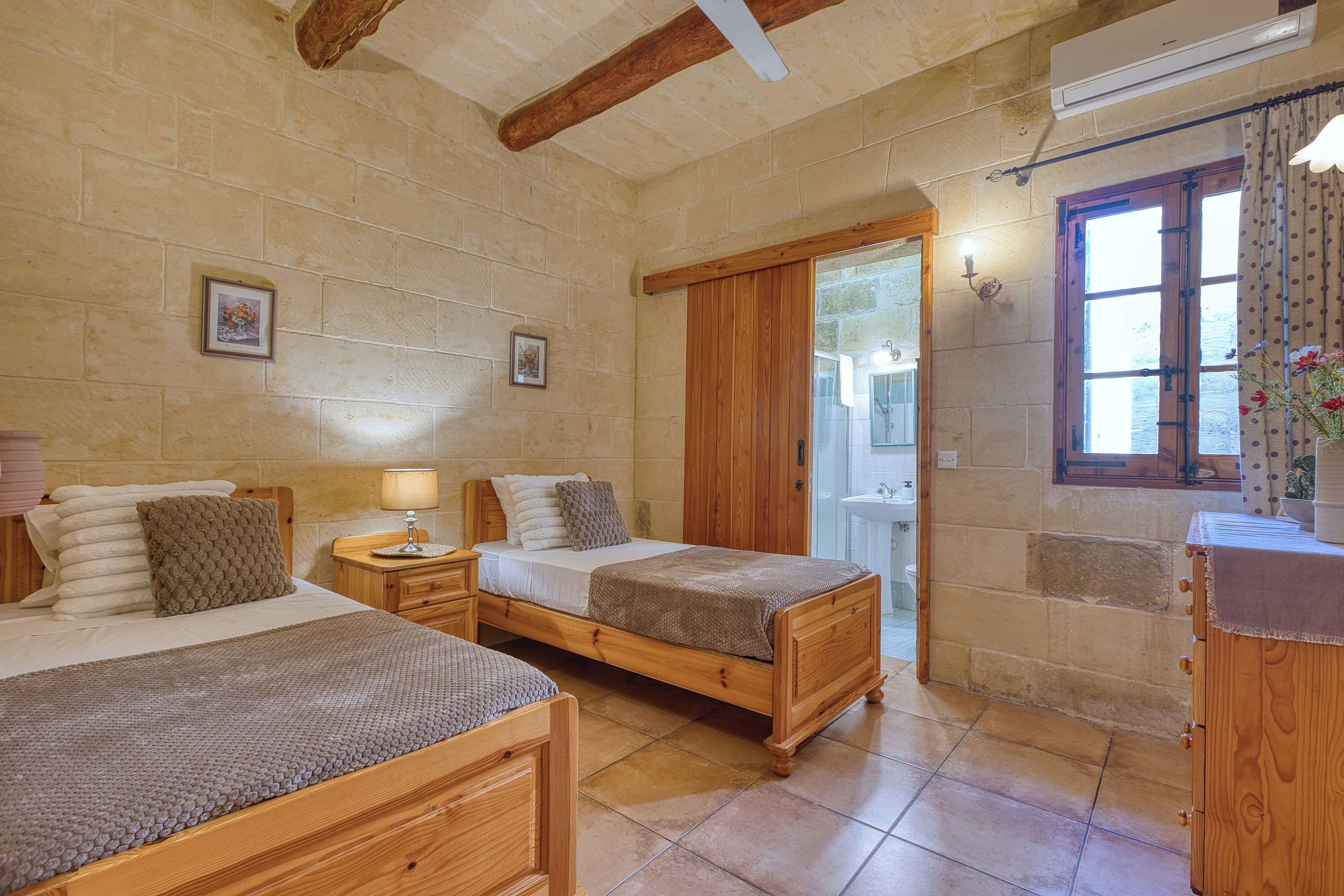 Una habitación con dos camas de madera, una mesita de noche, una lámpara de pared y un ventanal con cortinas.