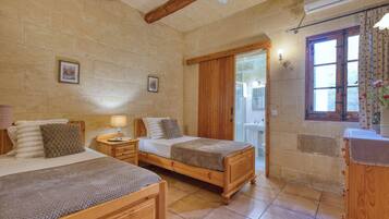 Una habitación con dos camas de madera, una mesita de noche, una lámpara de pared y un ventanal con cortinas.