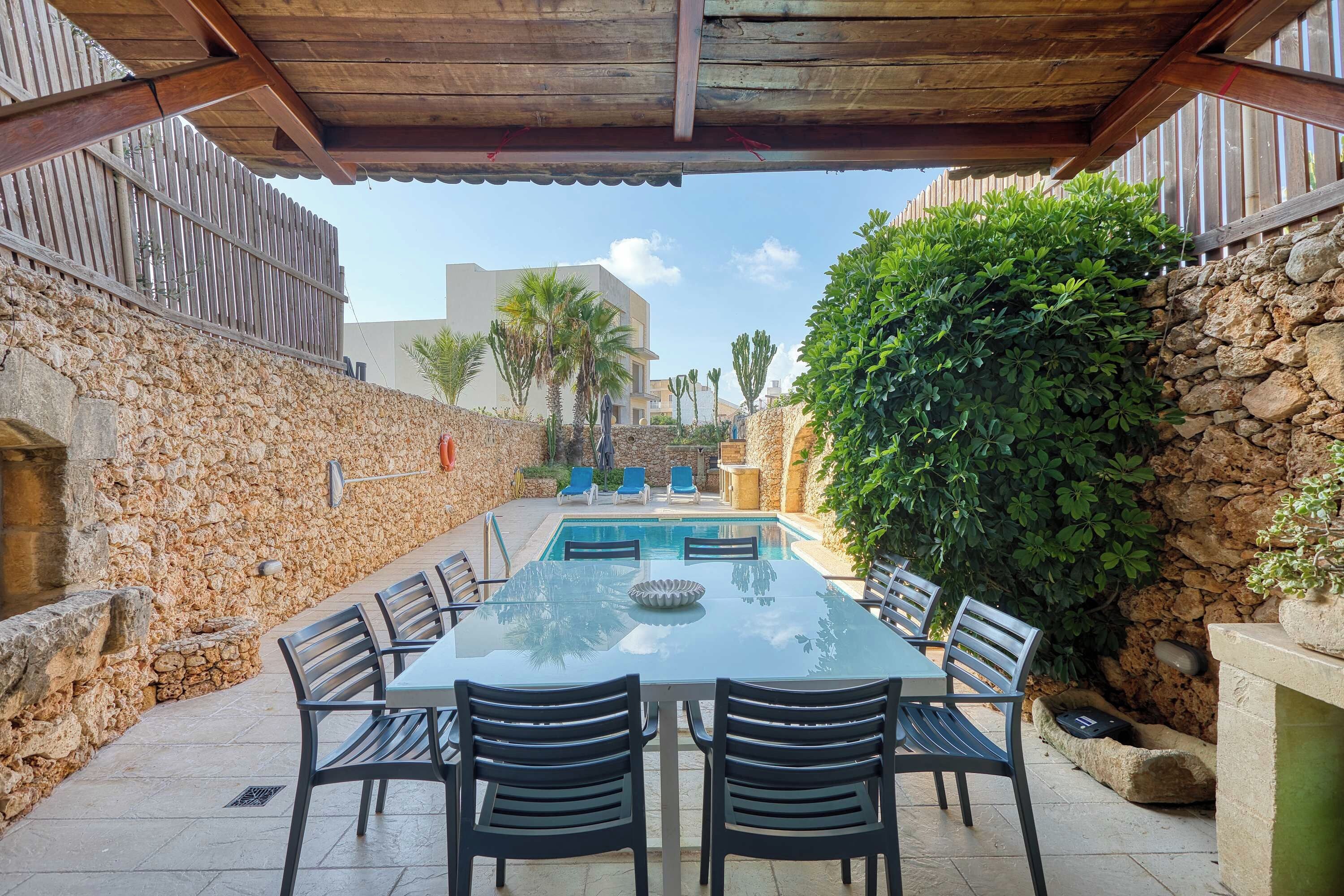 Un espacio al aire libre cubierto con piscina, paredes de piedra y una mesa con sillas.