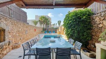 Un espacio al aire libre cubierto con piscina, paredes de piedra y una mesa con sillas.