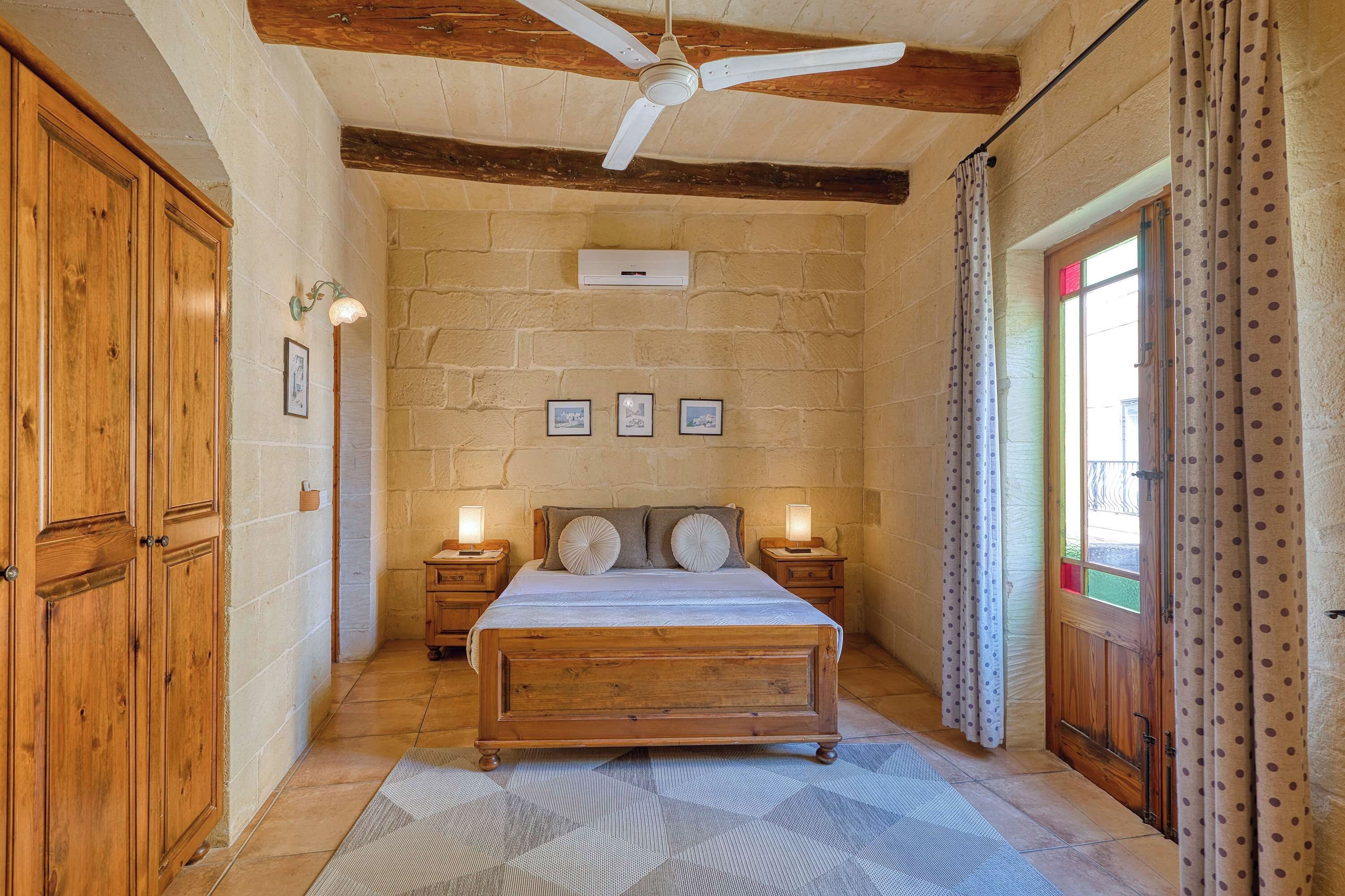 Un dormitorio con una cama de madera, un ventilador de techo y una pared de piedra.