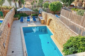 A swimming pool with a stone wall, a wooden fence, and a few lounge chairs. - Xaghra 5BDR Farmhouse with Pool by PMI Malta (Ix-Xagħra)
